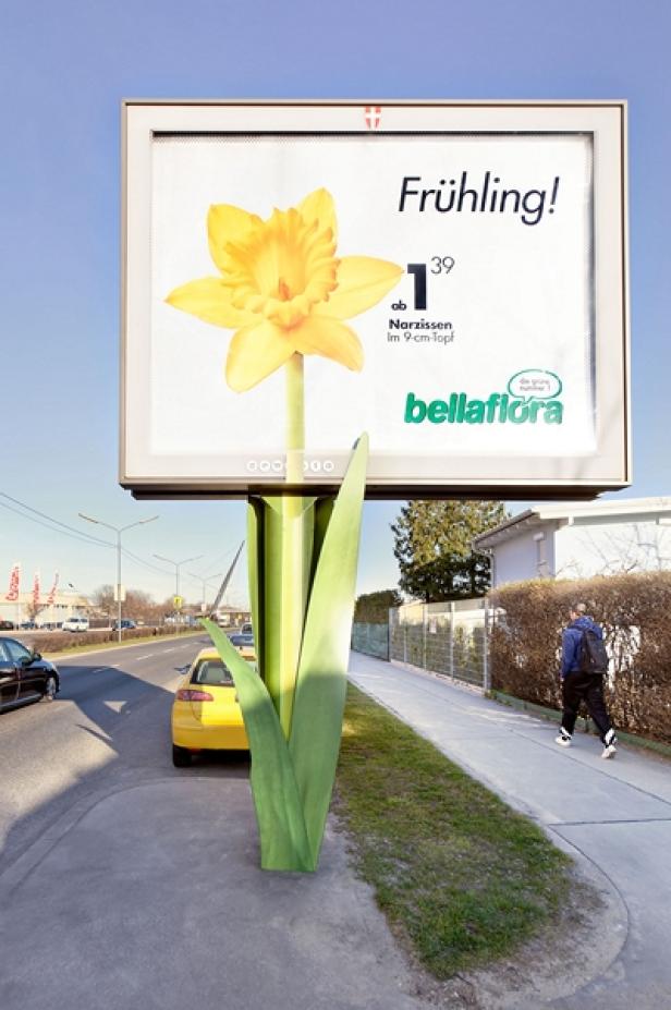 Eine Werbetafel in Form einer Narzisse wirbt für „bellaflora“ mit dem Slogan „Frühling!“.