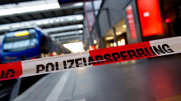 Ein rot-weißes Absperrband der Polizei vor einem Bahnhof.