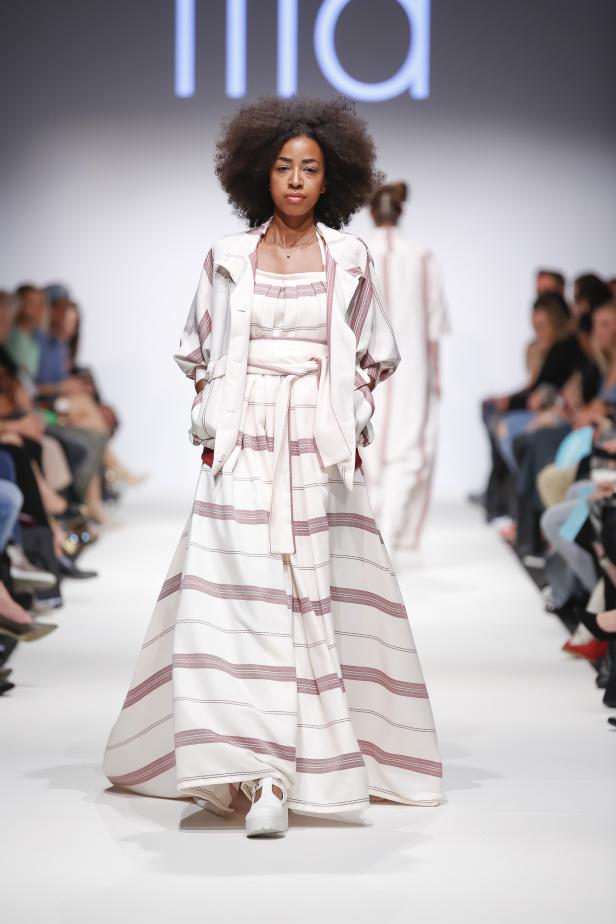 Eine Frau präsentiert ein langes, gestreiftes Kleid auf einem Laufsteg.