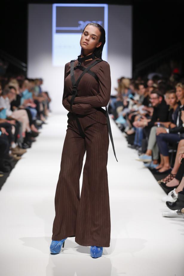 Eine Frau präsentiert ein braunes Hosenanzug mit Riemen auf einem Laufsteg.