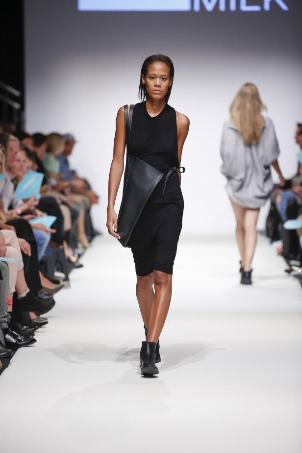 Eine Frau mit schwarzem Kleid und Tasche läuft auf einem Laufsteg.