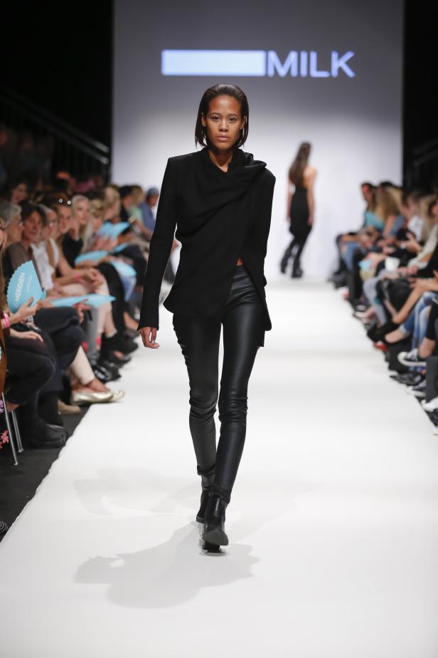 Eine Frau in schwarzer Jacke und Lederhose läuft über einen Laufsteg.