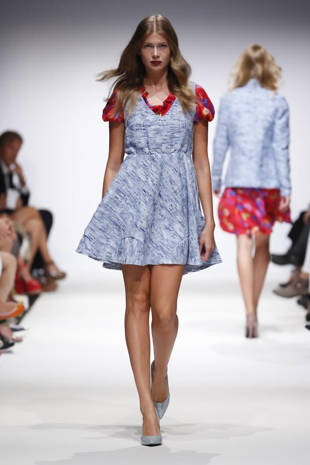 Eine Frau präsentiert ein blaues Kleid mit roten Akzenten auf einem Laufsteg.