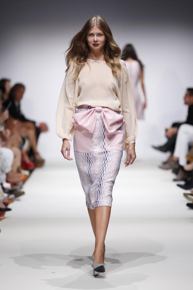 Eine Frau präsentiert ein Outfit mit einer Schleife auf dem Laufsteg.