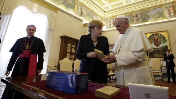 Angela Merkel überreicht Papst Franziskus ein Buch.