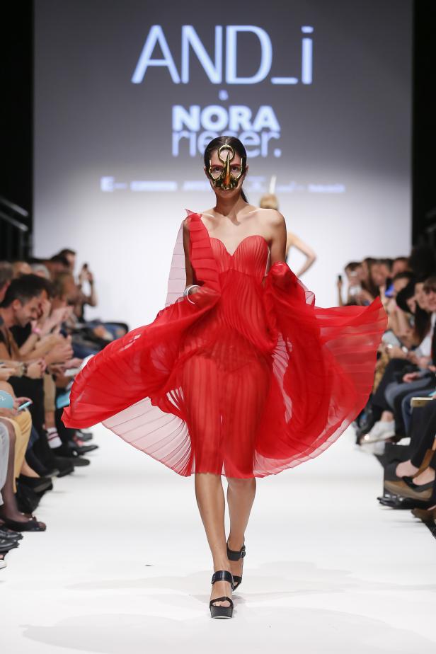 Eine Frau mit einer goldenen Maske und einem roten Kleid auf einer Modenschau.