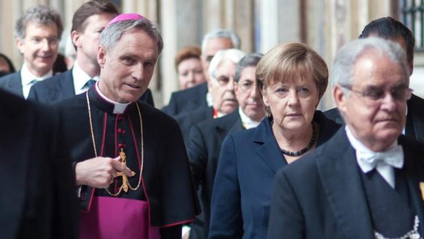 Angela Merkel bei einer Veranstaltung mit einem Bischof und anderen Würdenträgern.