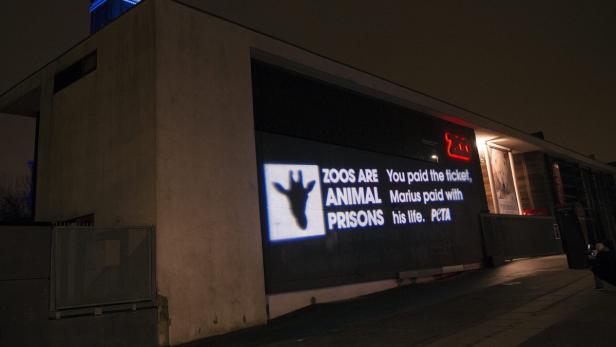 Eine Projektion an einem Gebäude mit der Aufschrift „Zoos are animal prisons“ und „Marius paid with his life. PETA“.