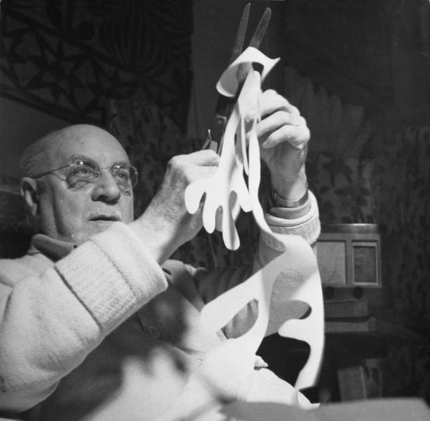 Henri Matisse schneidet Papierformen mit einer Schere.