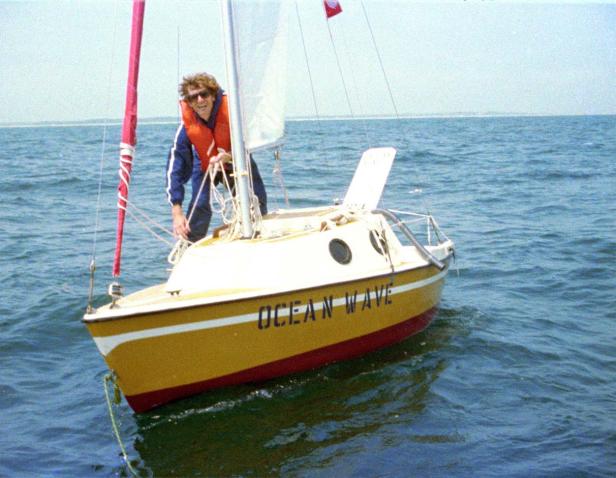 Ein Mann mit Schwimmweste segelt auf einem kleinen gelben Boot namens „Ocean Wave“.