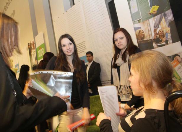 Mehrere Personen stehen vor Plakaten und lesen Dokumente.