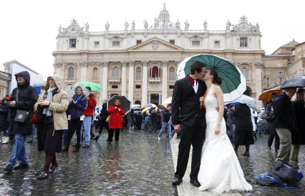 Ein Brautpaar küsst sich unter einem Regenschirm auf dem Petersplatz in Rom.