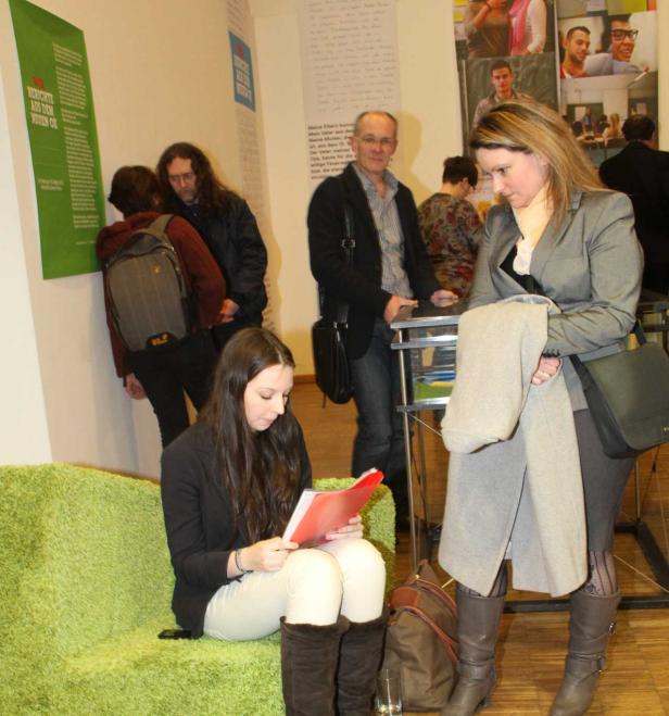 Mehrere Personen befinden sich in einem Raum mit Postern und lesen Dokumente.