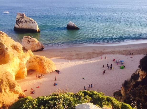 Blick von oben auf einen Strand mit Felsformationen und Badegästen.