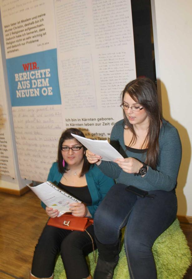 Zwei junge Frauen sitzen vor einer Wand mit Texten und lesen Papiere.