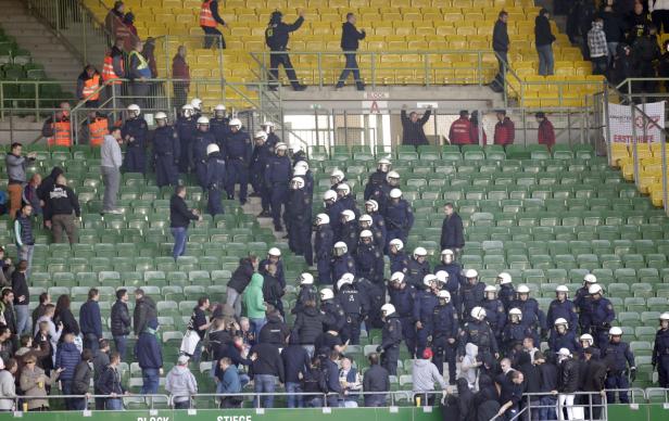 Polizisten in Helmen stehen in einem Fußballstadion zwischen den Zuschauern.