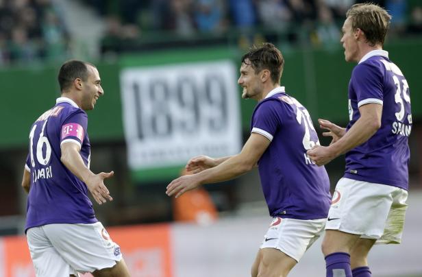 Drei Fußballspieler in lila Trikots jubeln auf dem Spielfeld.