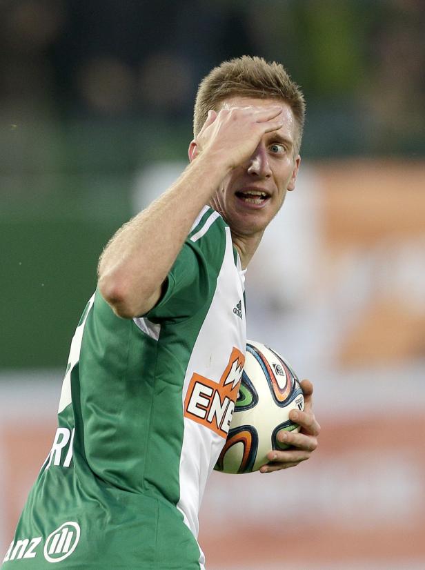 Ein Fußballspieler hält einen Ball und schützt seine Augen vor der Sonne.