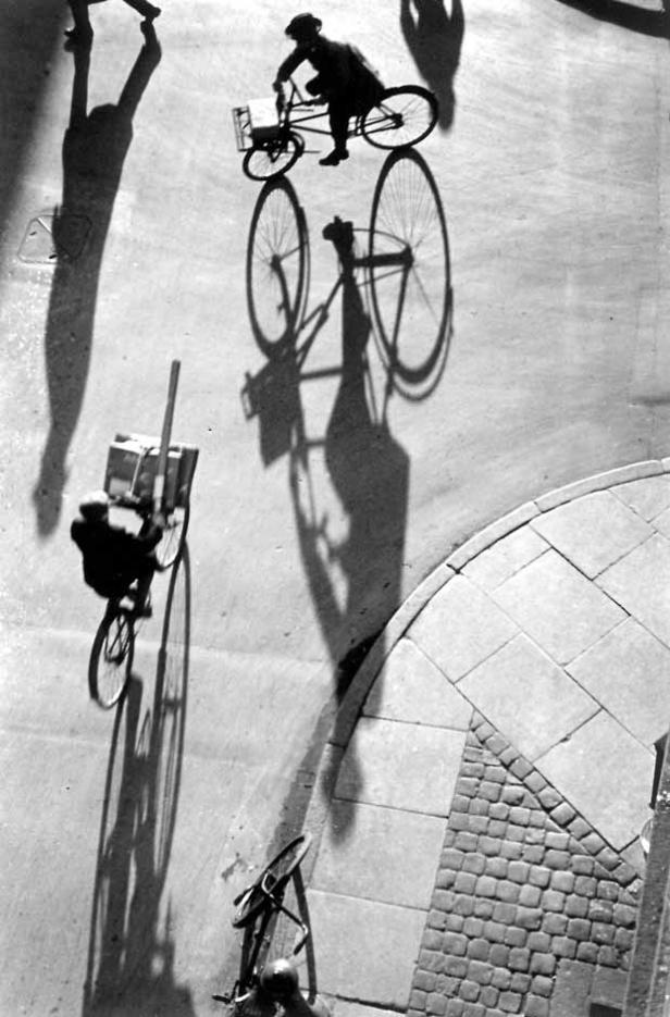 Draufsicht auf Radfahrer und Passanten, deren Schatten lange auf den Asphalt fallen.