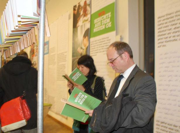 Zwei Personen lesen Broschüren mit dem Titel „Wir Berichte aus dem neuen OE“.