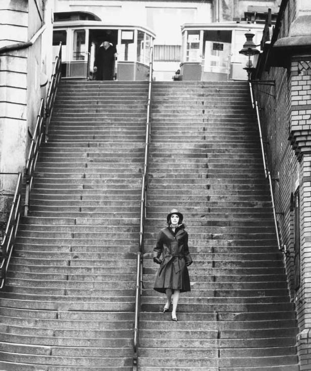 Eine Frau geht eine lange Treppe hinunter, im Hintergrund zwei Straßenbahnen.