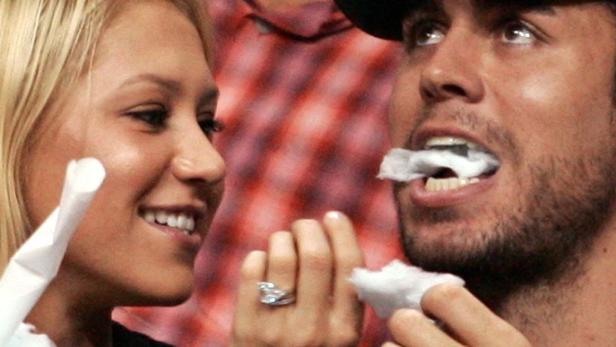 Anna Kournikova und Enrique Iglesias bei einer Veranstaltung, wobei Iglesias ein Papiertuch im Mund hat.