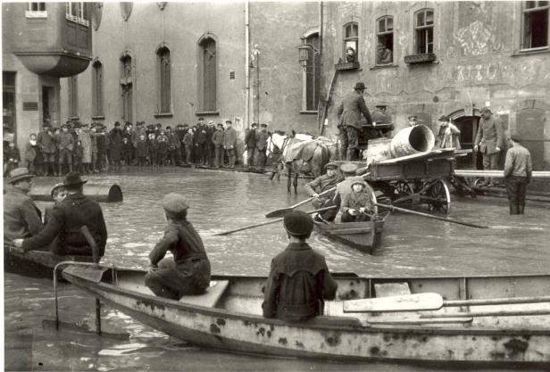 Historische Aufnahme einer Überschwemmung in einer Stadt, Menschen fahren mit Booten durch das Wasser.