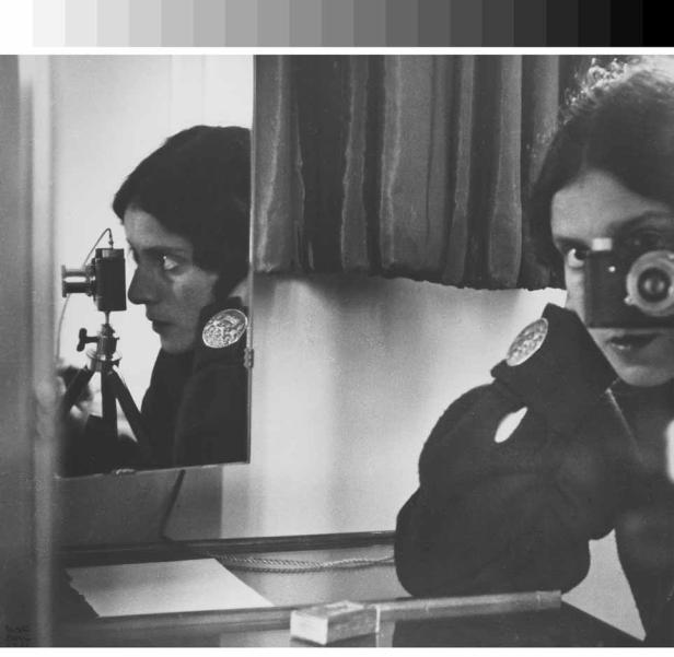Eine Frau fotografiert sich selbst im Spiegel mit einer alten Kamera.