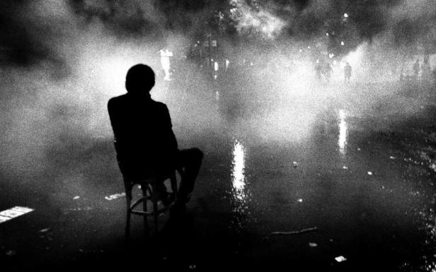Eine Person sitzt auf einem Stuhl im Nebel, der von Lichtern erhellt wird.