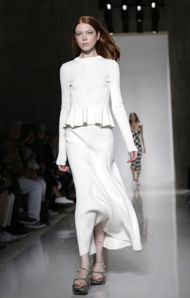 Ein rothaariges Model präsentiert ein weißes, langes Kleid auf dem Laufsteg.