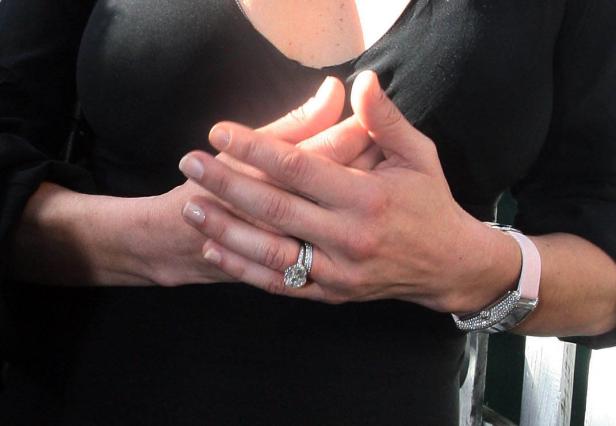 Die Hände einer Frau mit einem großen Diamantring und einer Uhr mit rosa Armband.