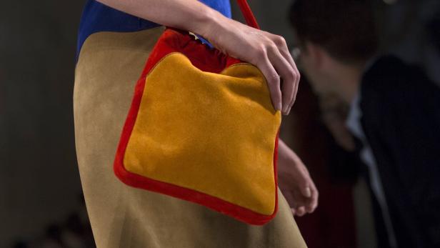 Eine Person hält eine orangefarbene Wildledertasche mit rotem Rand.