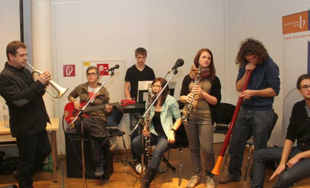 Eine Musikgruppe spielt verschiedene Instrumente, darunter Trompete, Bassgitarre, Klarinette und Didgeridoo.