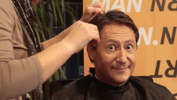 Ein Mann mit Frisierumhang bekommt die Haare gerichtet.