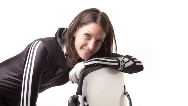 Eine Frau in Sportkleidung lehnt an einem Rennrodel.