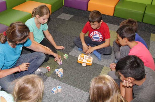 Eine Gruppe Kinder sitzt mit einer Betreuerin im Kreis und spielt mit Bauklötzen.