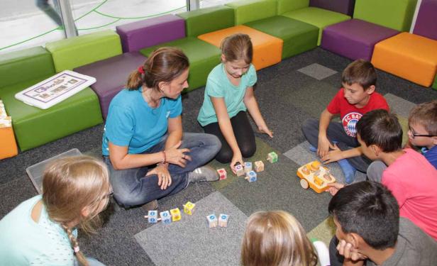 Eine Frau sitzt mit einer Gruppe von Kindern auf dem Boden und spielt mit Bauklötzen.