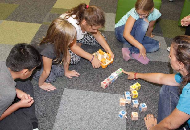 Eine Gruppe von Kindern und eine Frau spielen mit Bauklötzen auf dem Boden.
