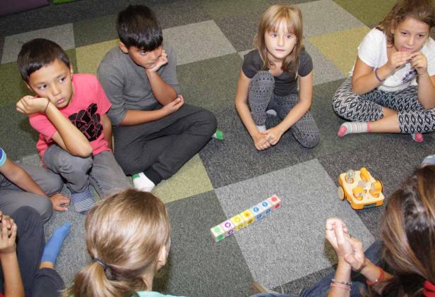 Eine Gruppe Kinder sitzt im Kreis auf einem Teppich und spielt mit Bauklötzen.
