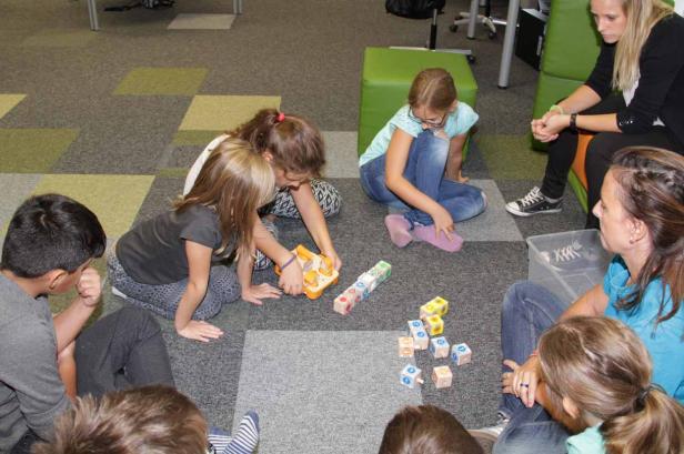 Eine Gruppe von Kindern sitzt mit zwei Erwachsenen auf dem Boden und spielt mit Bauklötzen.