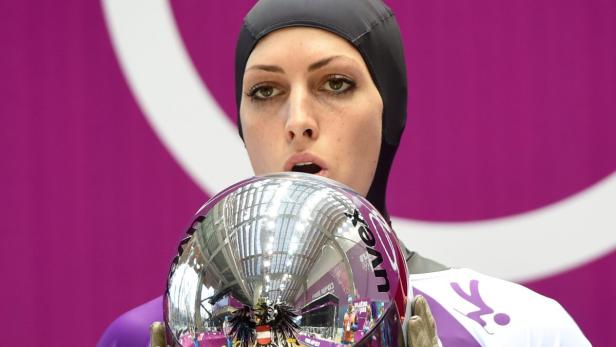 Eine Rennrodlerin hält ihren Helm vor einem violetten Hintergrund.