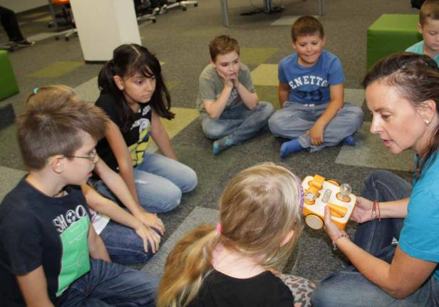 Eine Frau erklärt einer Gruppe von Kindern ein Spielzeug.