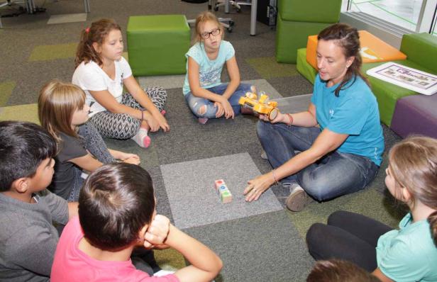 Eine Frau erklärt einer Gruppe von Kindern etwas mit Bauklötzen und einem Spielzeugauto.