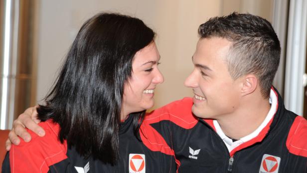 Ein lächelndes Paar in Trainingsjacken mit österreichischen Logos sieht sich an.