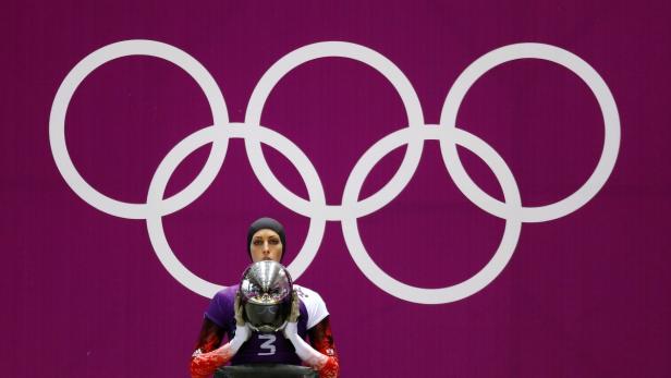 Eine Skeleton-Athletin hält ihren Helm vor dem Hintergrund der olympischen Ringe.