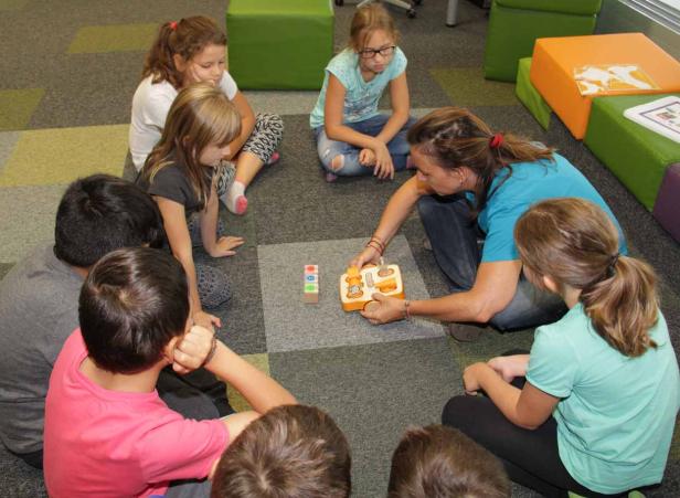 Eine Frau spielt mit einer Gruppe von Kindern auf dem Boden mit einem Spielzeug.