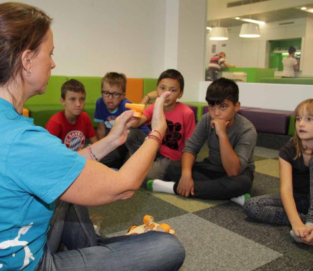 Eine Frau erklärt einer Gruppe von Kindern etwas mit einem Spielzeug in der Hand.