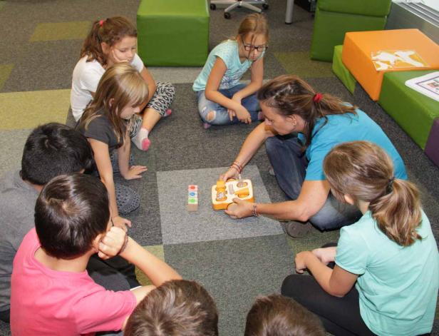 Eine Gruppe Kinder sitzt mit einer Betreuerin im Kreis und spielt mit einem Spielzeug.