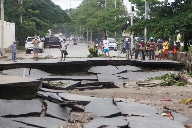 People stand near roads damaged by floods after heavy rains in Dili