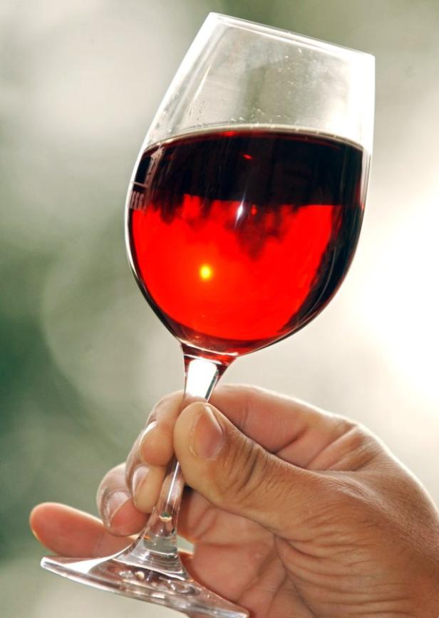 Eine Hand hält ein Glas Rotwein gegen einen hellen Hintergrund.